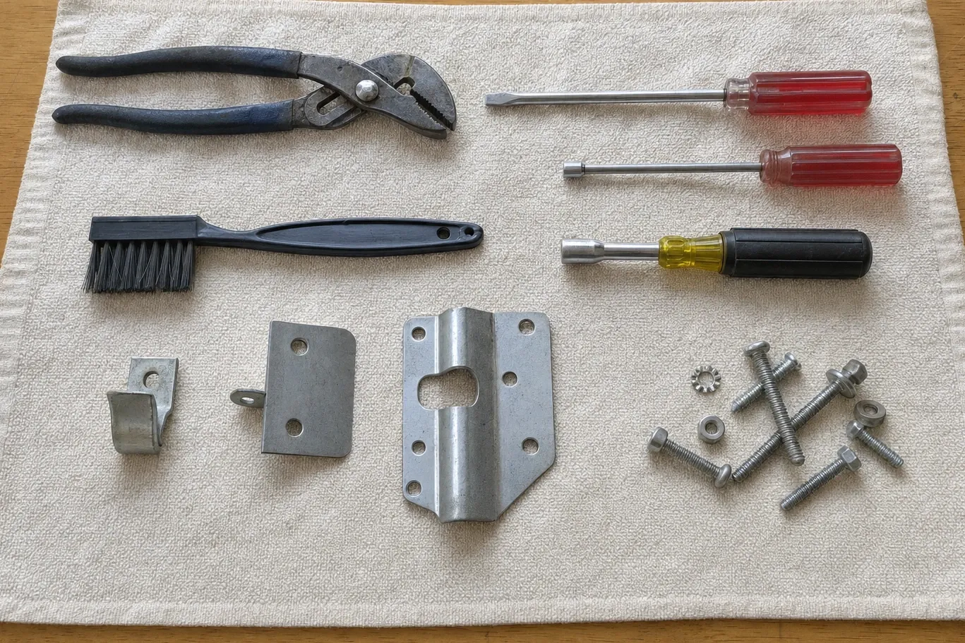 Tongue-and-groove pliers, nut drivers and four galvanised brackets with their bolts, laid out on a cloth